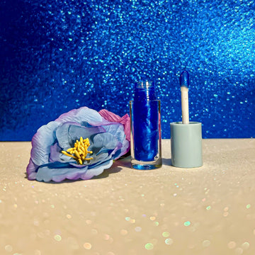 Coral Flavors Lip Gloss with applicator next to a blue and purple flower on a sparkly background.