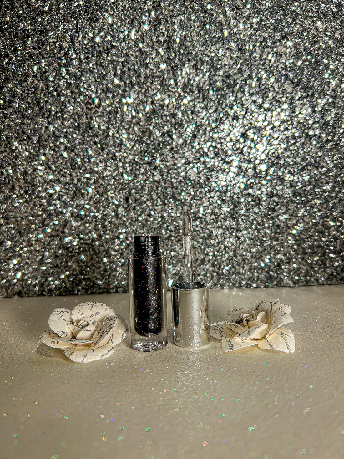 Sparkle Flavors Lip Gloss in a silver container with flowers, set against a sparkling backdrop.