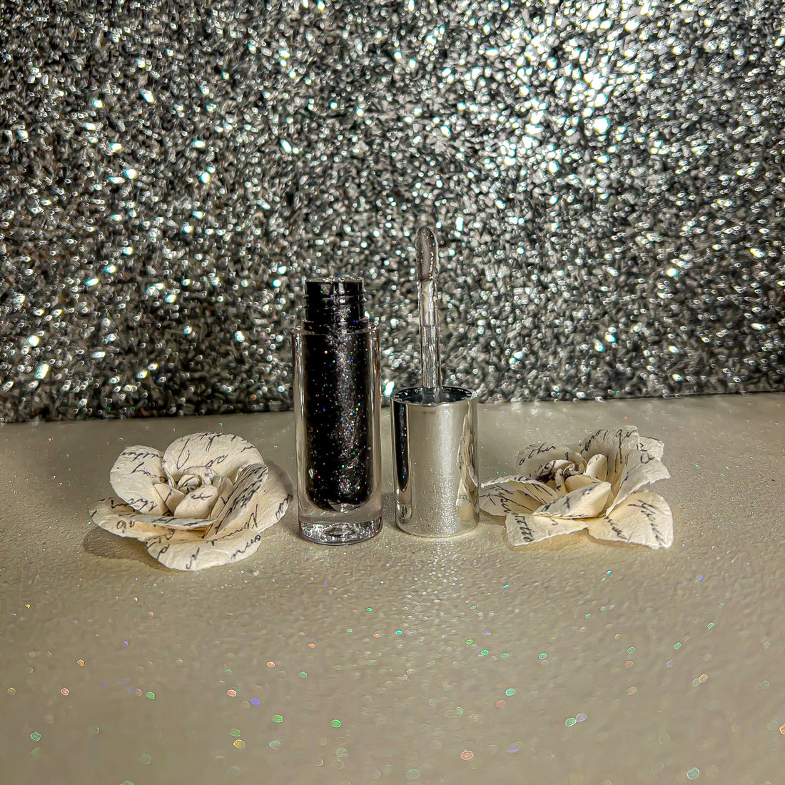 Sparkle Flavors Lip Gloss in a silver container with flowers, set against a sparkling backdrop.